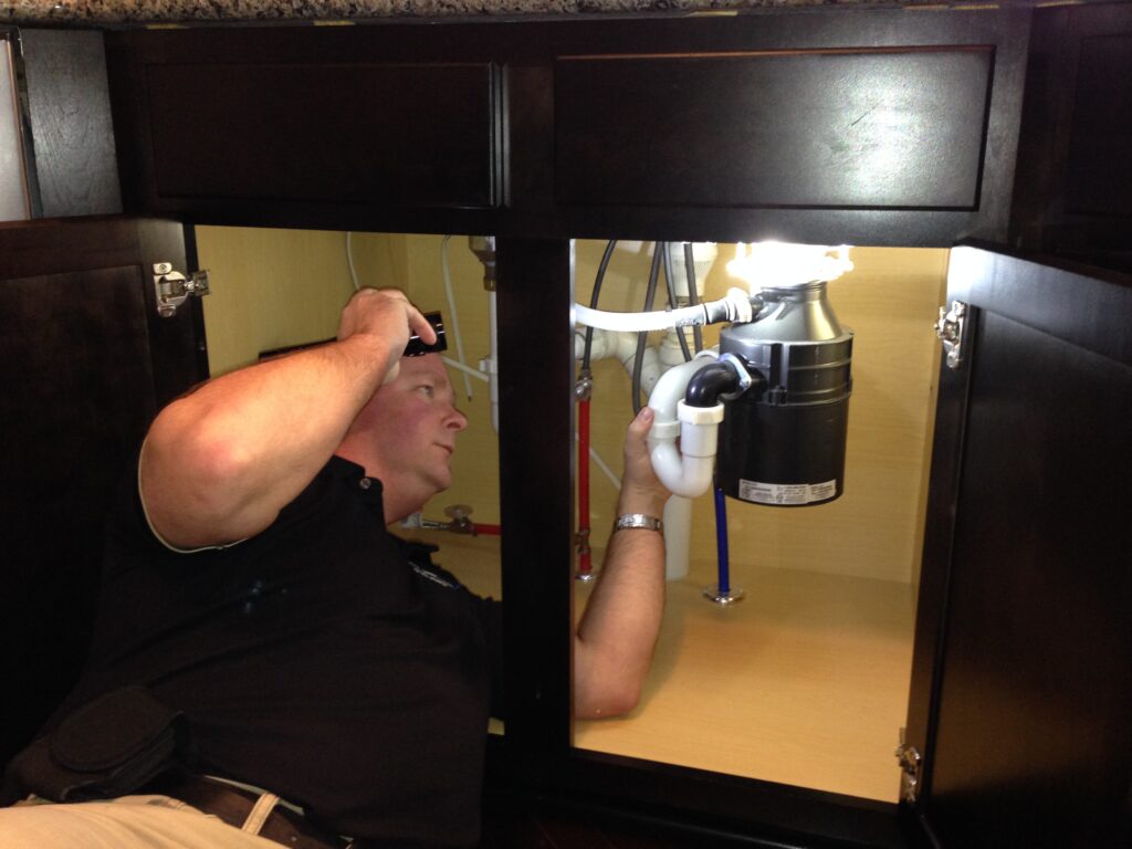 Dan Powell inspecting a garbage disposal under a kitchen sink during a home watch service visit in Rochester, NY