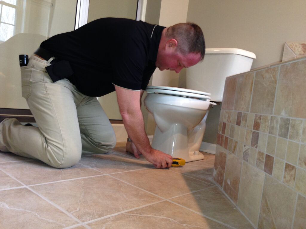 Dan Powell checks for water leaks around a toilet during a home watch visit in Rochester, NY